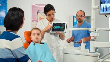 Stomatologist pointing on digital screen explaining x-ray to mother of girl patient. Doctor and nurse working together in stomatological clinic, examining, showing radiography of teeth on monitor photo