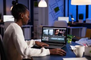 African american editor working late at night at digital movie project editing audio film montage in in creativity start-up business office. Videographer using post production software photo