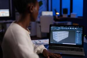 African american design arhitect working in 3D software developing prototype container idea working at night in corporate office. Technician engineer creating digital industrial project photo