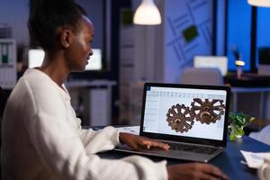 African american architect working industrial new project working at gear prototype late at night in start-up engineering office. Engineer woman developing technical construction product photo