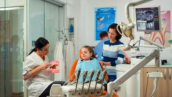 Stomatologist holding plaster model of the mandible speaking with girl patient. Dentist showing the correct dental hygiene using mock-up of skeleton of teeth, sample of human jaw with toothbrush photo