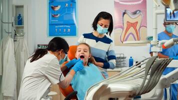 Stomatologist doctor checking tooth health of young patient using dental tools working in modern stomatological office with man nurse. Mother and daughter visiting doctor for periodic consulting photo