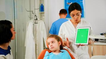 Stomatologist woman looking at green screen tablet while speaking with mother of little patient. Pediatric dentist explaining using monitor with green chroma key izolated chroma pc key mockup display photo