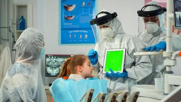 Dentist with face shield pointing at green screen display talking to child with toothache during coronavirus epidemic. Explaining using monitor with chroma key izolated chroma pc key mockup display photo