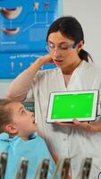 Dentist showing green screen display to mother of little patient while girl lying on dental chair. Woman explaining using monitor with green chroma key isolated chroma pc key mockup greenscreen photo