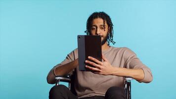 Person with paraplegia using tablet to post images on social media, doing selfie and writing photo caption. Man in wheelchair using online editing application on digital device, studio, camera A