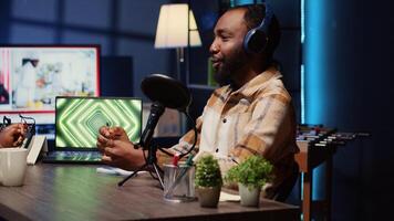 Guest on internet podcast show telling interesting story to host, captivating fans watching during live broadcast. African american man in studio sharing facts next to 3D animations running on laptop photo