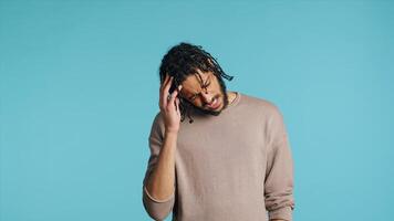 Hurt Middle Eastern man wincing from pain, suffering from headache, having health problems. Injured BIPOC person rubbing head temples, feeling discomforting strain, studio background, camera A photo