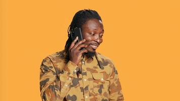 Cool person with braids answering phone call on camera, talking to friends or family in studio. African american trendy man chatting remotely with people, telephone line over background. photo