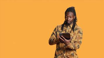 Modern person navigating online on tablet in studio, using mobile device to check social media apps and browse internet pages. African american man checking websites on gadget. photo
