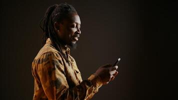 Modern person browsing online webpages on mobile phone, checking his socials for texts and posing in studio. African american man using smartphone apps to stay connected with friends. photo