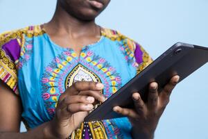 Female model of African American descent uses tablet to browse social networks and read articles from internet sources. Young woman in vintage traditional clothes searches web pages. photo
