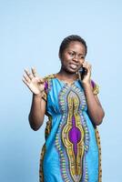 Positive enthusiastic woman is communicating with friends on mobile device in the studio. African american girl uses smartphone to have remote conversation, telephone connection. photo