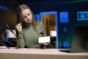 Young content creator filming technology review of newly released isolated screen smartphone, unpacking it and presenting specifications to audience. Internet star showing mockup mobile phone to fans photo