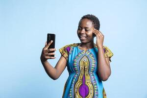 African american model attending online videoconference call, waving at her friends on videocall in studio. Cheerful woman feeling happy while she is having a remote discussion on web network. photo