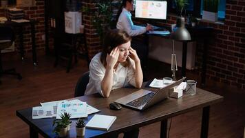 Tired employee struggling to remain focused at workspace desk, feeling overworked and waiting to go home. Bored businesswoman sighing in office while working overnight, camera A photo