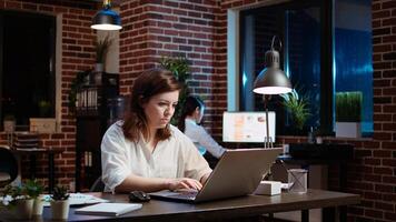 Businesswoman working overtime for company project, doing tasks in office overnight. Employee looking over accounting figures on laptop screen late at night, inputting data photo