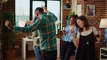 Young adults of various nationalities dancing at home party while drinking alcohol. Friends hanging around, having good time together while enjoying upbeat music in living room photo