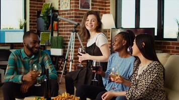 Multicultural friends having fun together, enjoying alcohol drinks and snacks in cozy apartment living room, gathered together for celebrations. BIPOC group of people chatting at home photo