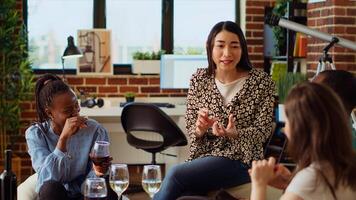 Asian woman entertaining friends at apartment party, sharing with them funny tale. Guest making multiethnic group of people laugh in living room while drinking alcoholic beverages photo