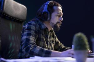 Focused man brings his laptop to virtual meetings and surfs the internet with wireless headphones on. Bearded guy who multitasks by watching movies and doing online homework. photo