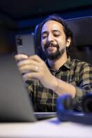 Joyful man holding his smartphone and having an online conversation with friends and family. Thrilled guy using his cell phone to browse the internet and find humorous posts on social media. photo