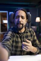 Male influencer interacts with his social media groups live on the internet while pointing at the camera. Point of view of an individual using a mobile device to record a at home. photo
