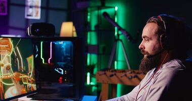 Happy man using headphones mic to communicate with online friends from his dark living room, playing engaging games on gaming PC at computer desk, relaxing after work photo