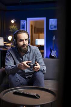 Gamer using headphones mic to discuss with teammates while playing games and enjoy leisure time. Excited man in apartment entertained by videogame on console, using gamepad photo