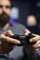 Focus shot on controller held by man defeating enemies while playing videogames on gaming console with teammates. Player in blurry background using gamepad to participate in esports game photo