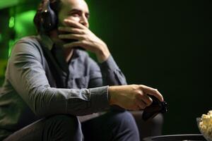 Man having fun and laughing while playing games on gaming console, talking with teammates using headphones mic. Happy gamer battling rival players using controller, amused by friends during chat photo