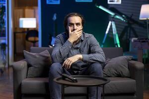 Viewer gasping while watching horror television series on streaming service, enjoying time off from work. Astonished person covering mouth in disbelief, shocked by film scene broadcasted on TV photo