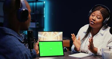 Woman invited to podcast watching internet clips on green screen tablet with host in studio, discussing content. African american guest reacting to videos on mockup device during online comedy show photo