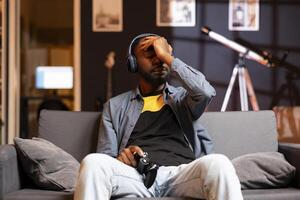 Man putting palm on forehead, feeling headache coming after receiving game over while playing videogames on gaming console. Gamer on couch getting high tension after being defeated photo