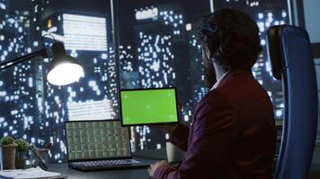 Private equity associate uses greenscreen display on tablet, sitting at workstation inside skyscraper. Influential chairman looks at gadget with blank copyspace template screen, legal work. photo