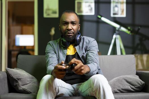 Gamer showing concern after being outsmarted by enemies while playing videogames on console. African american man feeling annoyed after being defeated while playing games with gamepad photo