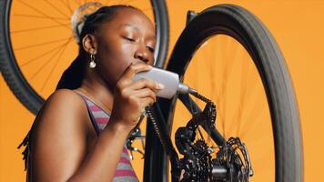 BIPOC mechanic using specialized glue to fix damaged bicycle chain, orange studio background. Expert applying adhesive on bike parts during checkup process, close up shot photo