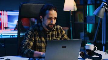 Freelancer sitting at home office desk and typing on laptop keyboard, doing his job. Remote worker using electronic device to send emails to customers from living room, camera A photo