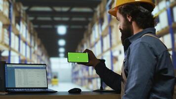 Warehouse manager looks at greenscreen on smartphone display, working on parcel shipment and delivery in industrial depot. Quality control advisor using blank copyspace mockup screen. photo