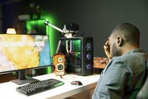 Gamer losing intense singleplayer spaceship arcade racing videogame, seeing game over screen on gaming computer monitor. Man being upset after being destroyed on difficult SF game level photo