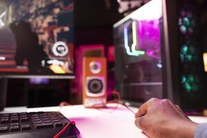 Gamer using keyboard and mouse to play FPS videogame on gaming PC tower with neon lit components. Man in apartment at night using high tech computer peripherals to defeat foes, close up photo