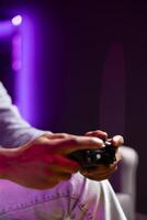 Gamer in neon lit apartment using controller to play videogame at home, close up. Man in RGB illuminated home using high tech gaming console gamepad to defeat opponents in game photo