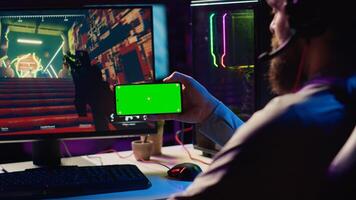 Man watching tutorial on isolated screen phone while playing first person shooter videogame with gun shooting laser bullets. Gamer learning to play game by looking at online guide on cellphone photo
