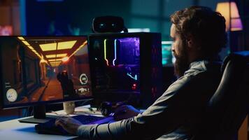 Portrait of smiling man in dimly lit apartment playing games on gaming PC at computer desk, enjoying day off from work. Gamer battling enemies in online multiplayer shooter photo