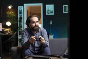 Joyous man playing videogame in home theatre, holding controller. Smiling gamer participating in PvP online multiplayer game using console system and high quality gamepad photo