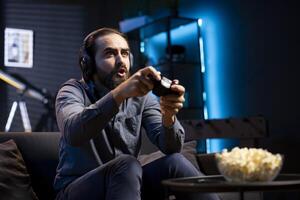 Man showing surprise facial expression while playing videogames on gaming console with teammates. Player acting shocked after being defeated by foes in game, discussing with friends through headset photo