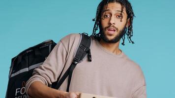 Portrait of BIPOC courier delivering pizza order to client. Delivery part time worker using thermal backpack to store food and bring it to customer, isolated over studio background, camera B photo