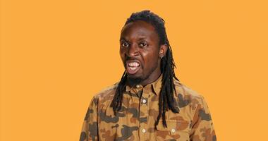 Confident adult screaming in front of camera in studio, feeling furious and angry. African american person showing rage and yelling, aggressive mad guy with dreads. Handheld shot. photo