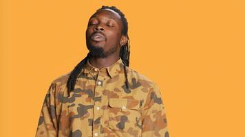 Male model inhaling and exhaling in studio, showing breathing exercises for wellbeing over orange background. Young athletic adult taking breaths and relaxing on camera. Handheld shot. photo