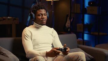African american man playing videogames on console late at night, struggling to stay awake. Gamer using joypad controller to try and finish singleplayer game level before going to sleep. photo
